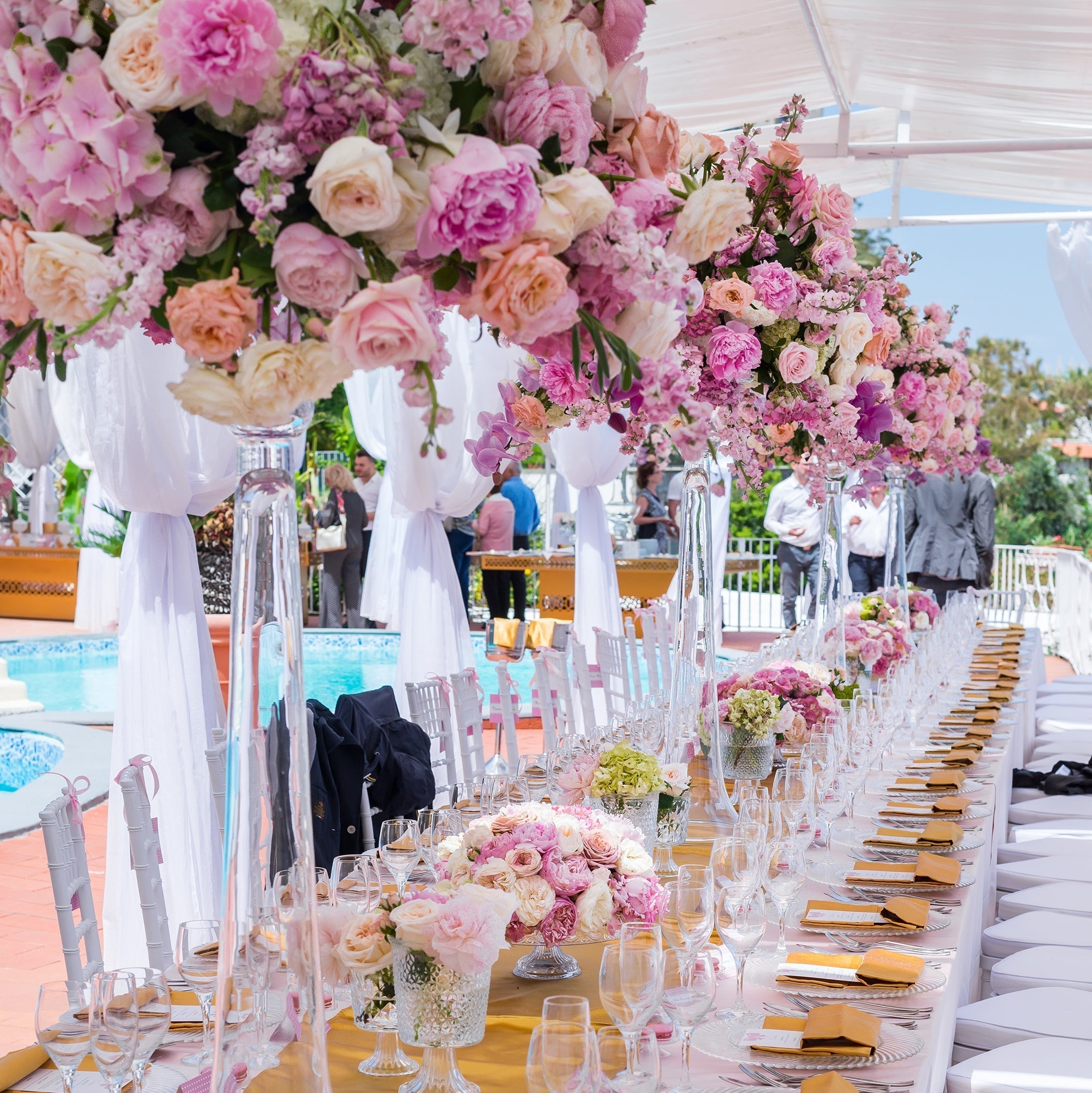 Long table set for a formal event with pink floral arrangements, white tablecloth, and yellow napkins.