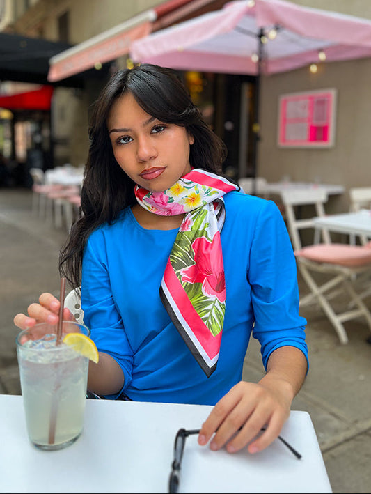 Woman sitting at an outdoor cafe table with a drink, wearing a colorful scarf.